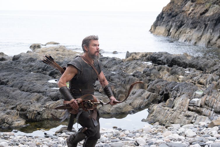 Matt Damon como Odiseo corriendo a lo largo de una costa escarpada.