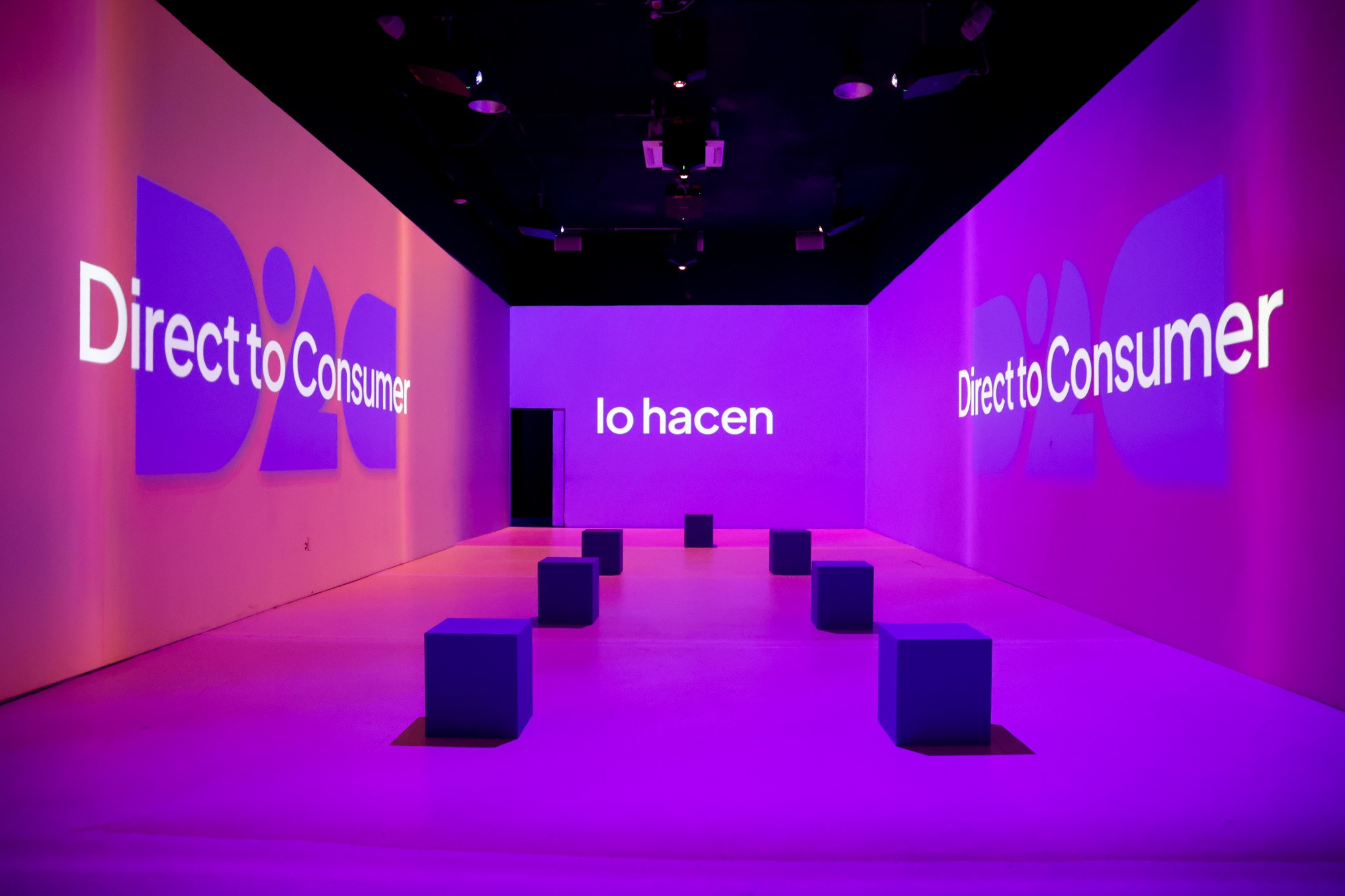 Sala del D2C Summit con proyecciones de Direct to Consumer en las paredes y asientos cúbicos.