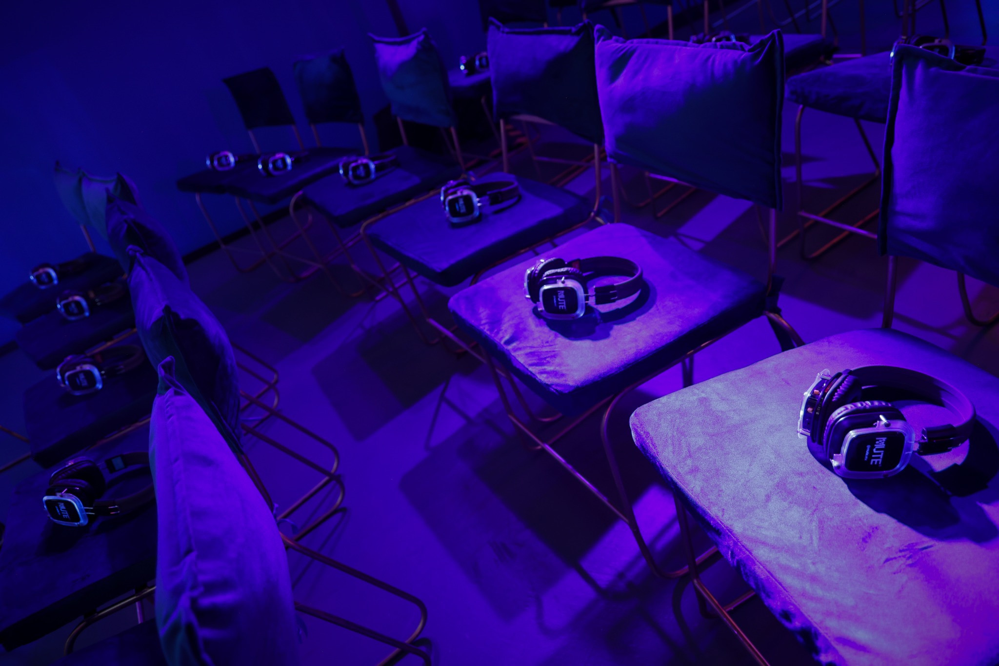 Audífonos sobre los asientos de una sala del D2C Summit iluminada en tonos violetas.